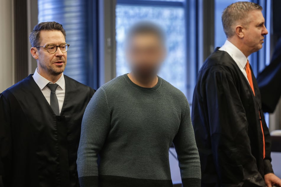 Der Angeklagte (M) steht im Gerichtssaal zwischen seinen Anwälten Boris Kröning (l) und Peter Krieger (r).