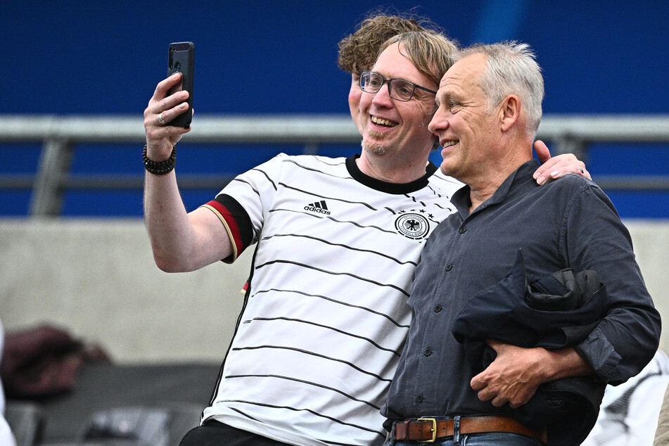 Der ehemalige Trainer des SC Freiburg Christian Streich (r.) schießt vor dem Anpfiff noch ein Selfie mit einem Fan.