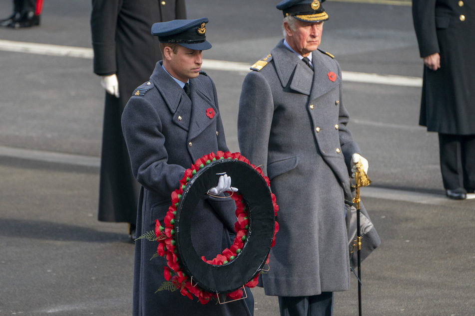 Prinz William (l), Herzog von Cambridge, hält bei der Gedenkfeier neben Prinz Charles, Prinz von Wales, einen Mohnblumenkranz in der Hand.
