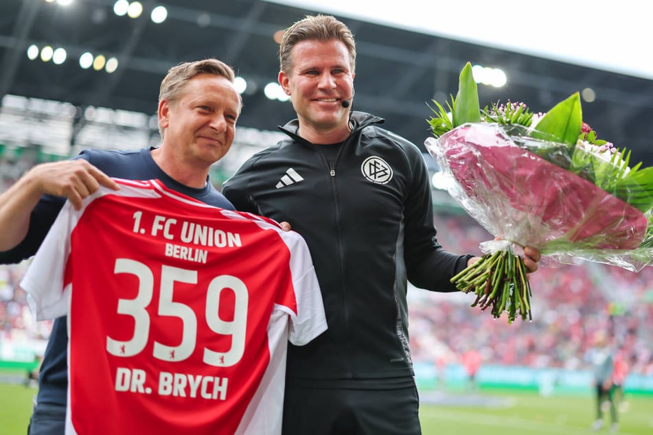Union-Manager Horst Heldt (l.) überreicht Schiedsrichter Felix Brych vor dem Anpfiff ein Trikot mit der Nummer 359 - der Anzahl seiner Bundesliga-Spiele.
