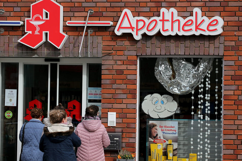 Menschen warten vor einer Apotheke in Gangelt, bei der nur durch den Nachtschalter bedient wird.