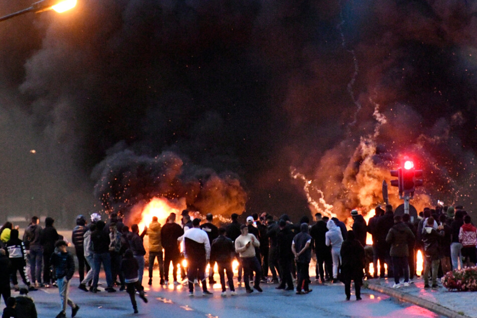 Demonstranten stehen auf einer Straße vor brennenden Reifen.