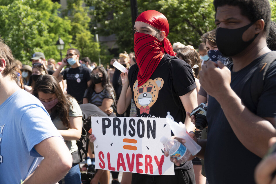 A demonstrator raises a sign reading "Prison = Slavery" during a New York City protest against police brutality, mass incarceration, and systemic racism.