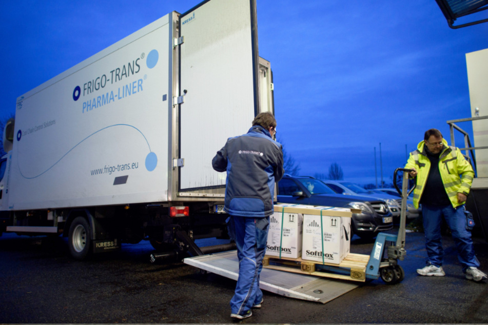Fahrer eines Kühllastwagens entladen in einem Logistikzentrum Kisten mit Impfdosen von Biontech/Pfizer.