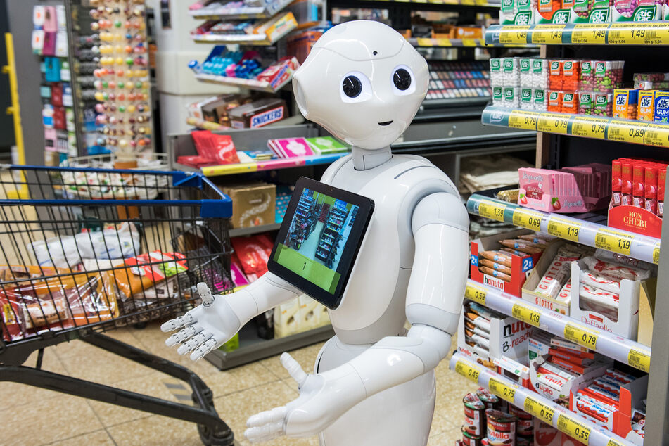Der humanoide Roboter mit dem Namen "Pepper" steht in einem Supermarkt vor den Kassen.