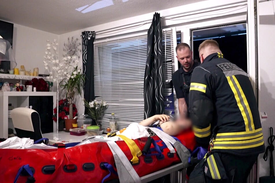Die Patientin wird mithilfe der Feuerwehr auf einer Trage aus dem Haus auf die Feuerwehr-Drehleiter transportiert.