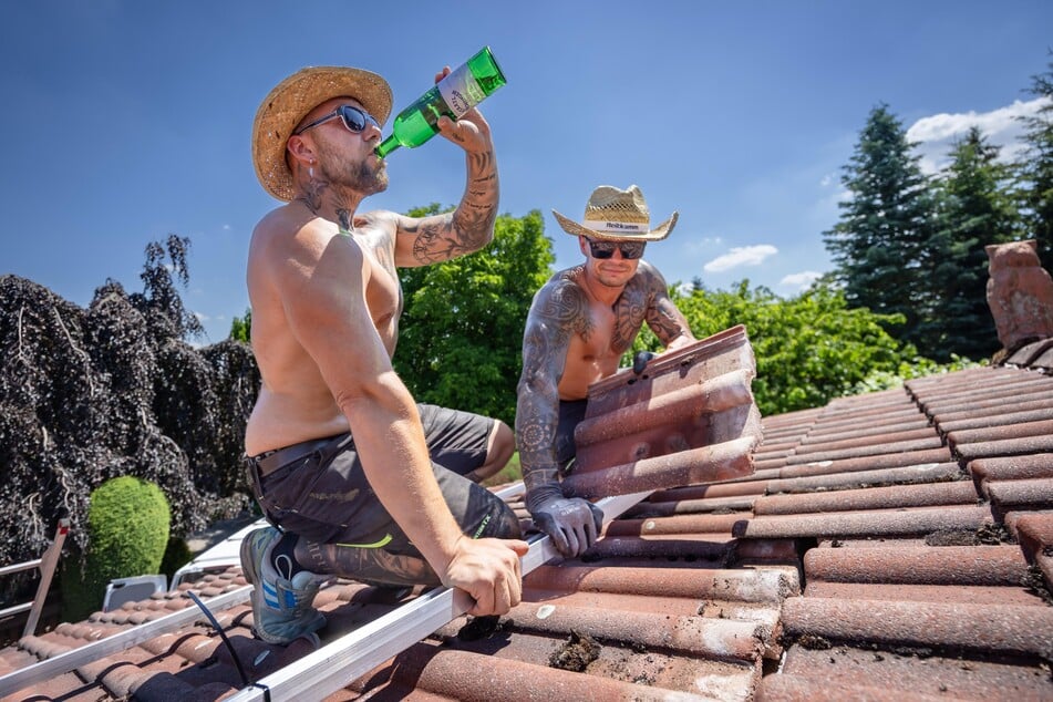 Die Dachdecker Christian (35, l.) und Sebastian (37) montieren in praller Sonne auf einem Dach Solarpaneele.