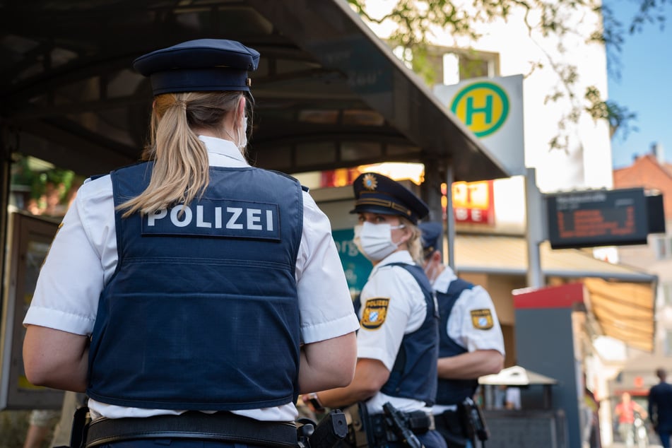Drei Polizisten stehen an einer Tram-Haltestelle.