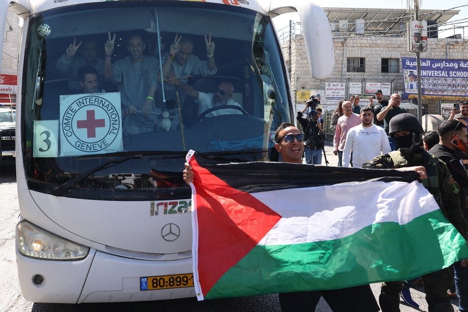 A man holds up a Palestinian flag in front of a bus carrying people recently released from Israel's Ofer military prison in the illegally occupied West Bank on October 13, 2025.
