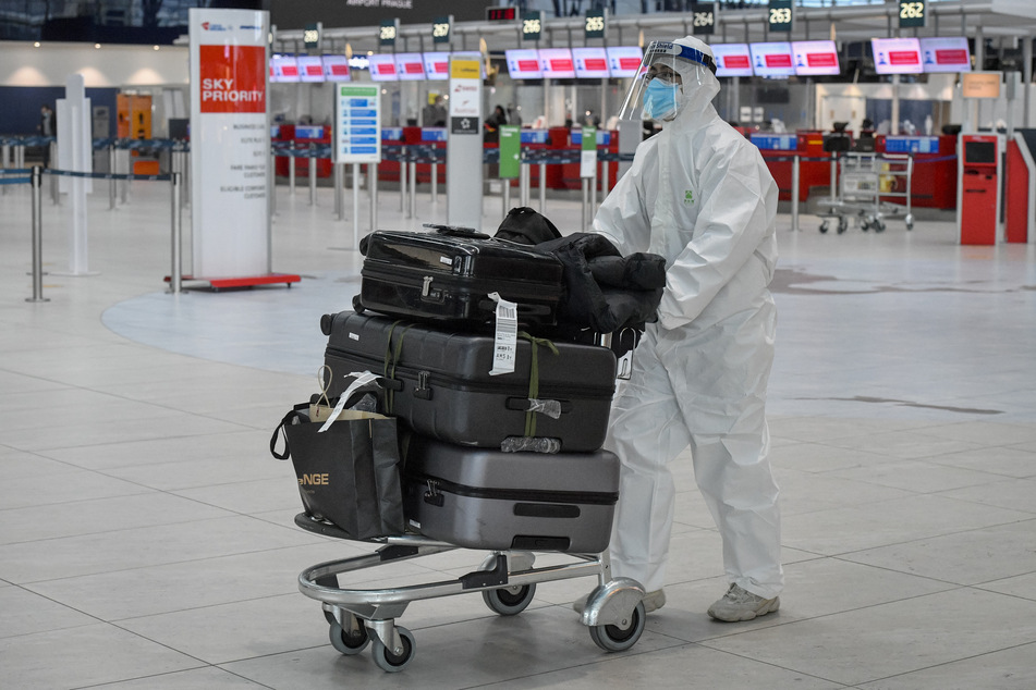 Tschechien, Prag: Ein Passagier, der zum Schutz vor dem Coronavirus einen Schutzanzug, Mund-Nasen-Schutz und Gesichtsvisier trägt, schiebt einen Gepäckwagen durch die Abflughalle des Flughafens Prag.