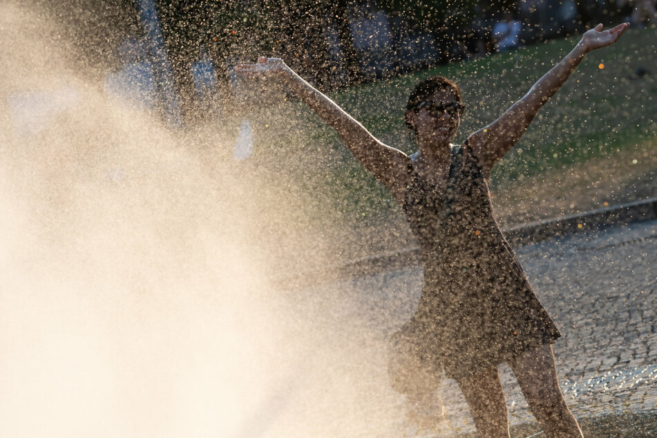 Eine Frau freut sich zwischen den Fontänen des Brunnens im Lustgarten über Abkühlung beim heißen Sommerwetter.