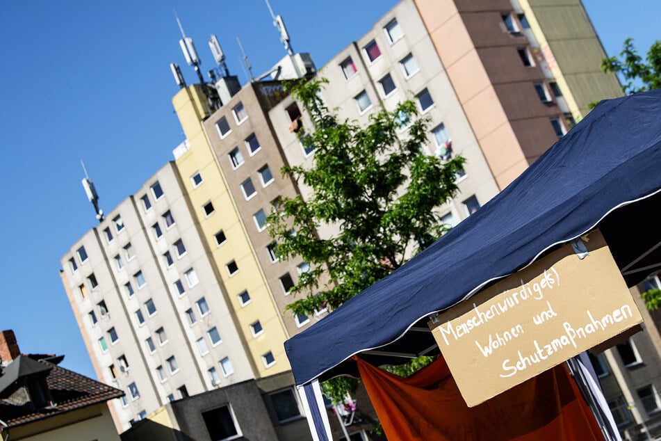 "Menschenwürdige(s) Wohnen und Schutzmaßnahmen" steht auf einem Plakat vor einem unter Quarantäne gestelltem Wohngebäude.