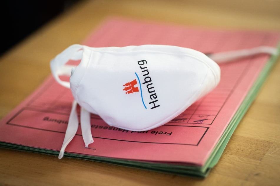 Eine Mund-Nase-Bedeckung mit Hamburg-Logo liegt auf einer Dokumentenmappe bei einer Pressekonferenz in einer Grundschule.