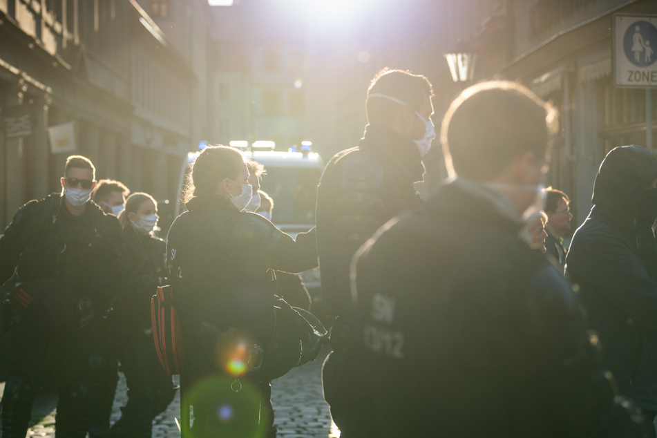 Polizisten stehen am Rand einer Demonstration von Gegnern der Corona-Maßnahmen auf dem Marktplatz von Pirna in einer Seitenstraße.