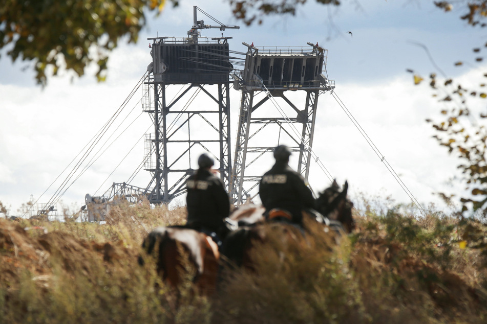 Polizisten reiten an einem Braunkohlebagger vorbei. (Symbolbild)