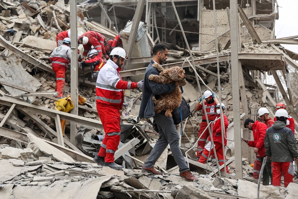 A man carries a dog as emergency personnel work at the site of a strike on a residential building in Tehran, Iran, on March 16, 2026.