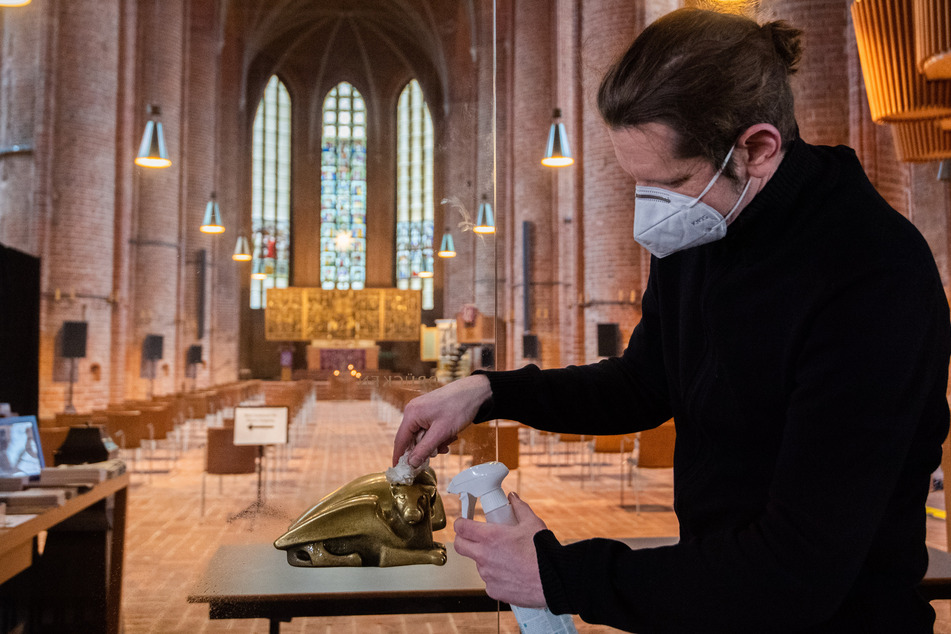 Ein Küster desinfiziert den Griff einer Glastür in einer Kirche.