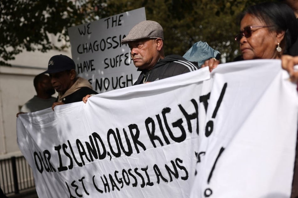 Members of the Chagossian community gather with banners and signs in a protest outside the UK parliament.