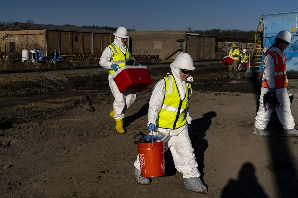 EPA contractors walk back to their cars with collected soil samples from the East Palestine derailment site.