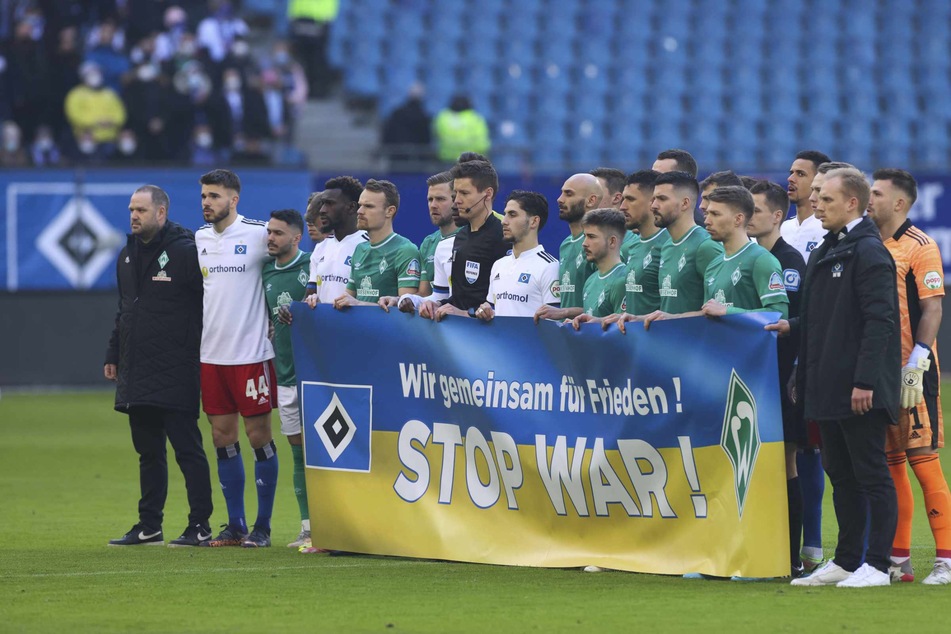 Die Spieler beider Mannschaften stehen vor dem Spiel während einer Schweigeminute für die Ukraine zusammen, und halten ein Banner mit der Aufschrift "Wie gemeinsam für Frieden! stop war!"