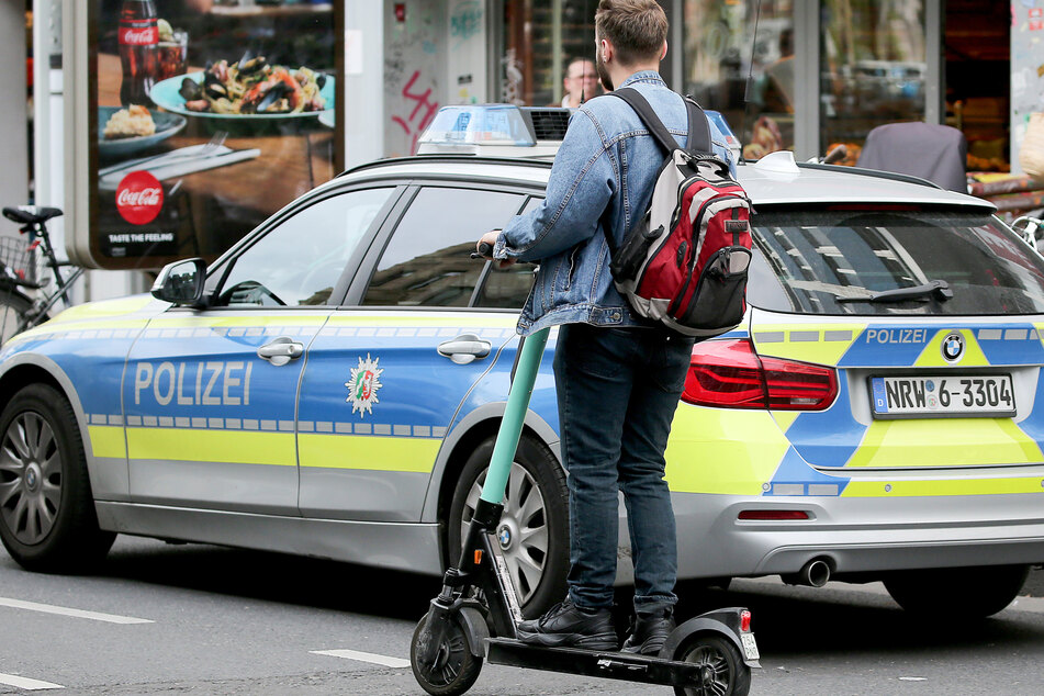 Ein E-Scooter-Fahrer fährt an einem Polizeiauto in Köln vorbei.