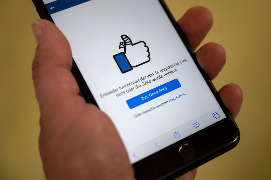 Ein Mann hält ein Smartphone in der Hand, auf dem eine Facebook-Seite zu sehen ist.