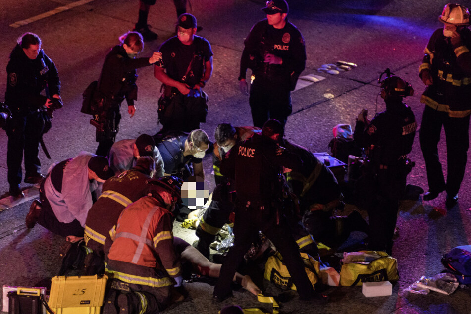 USA, Seattle: Rettungskräfte kümmern sich um die verletzte Person am Boden, nachdem ein Fahrer laut Behörden in eine protestbedingte Barrikade auf der Autobahn Interstate 5 gefahren ist.