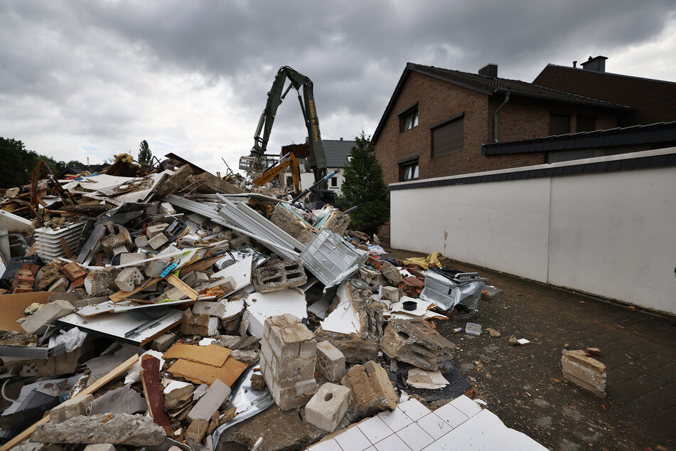 Ein Bagger reißt in Erftstadt-Blessem hinter einem Müllhaufen ein Haus ab.