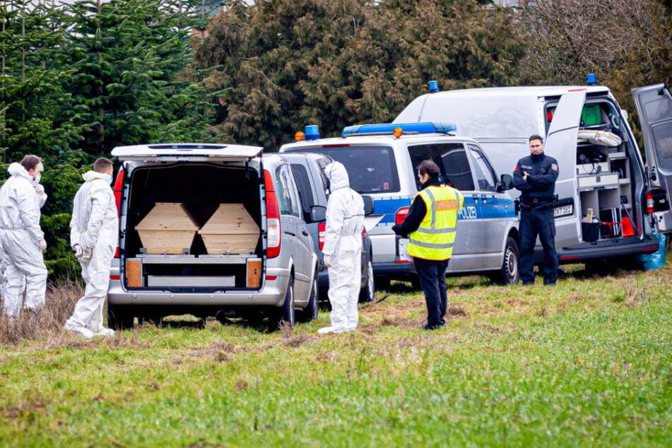Mitarbeiter der Spurensicherung der Polizei stehen an einem Leichenwagen, der auf einer Wiese parkt. Dort wurde die Leiche des vermissten 14-Jährigen gefunden.