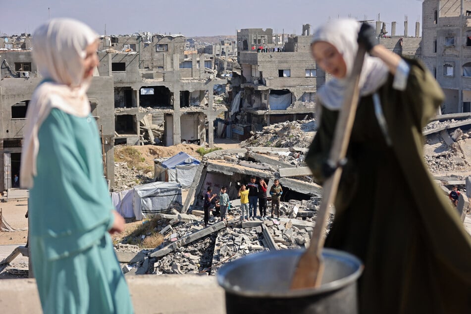 Displaced children stand on the rubble of destroyed houses as they watch the food being prepared on the rooftop of the house of Palestinian sisters Lina Zeid (l.) and Aya Zeid, who distribute food as a charity in the Al-Tuam area, west of Jabalia in the northern Gaza Strip, on May 6, 2026.
