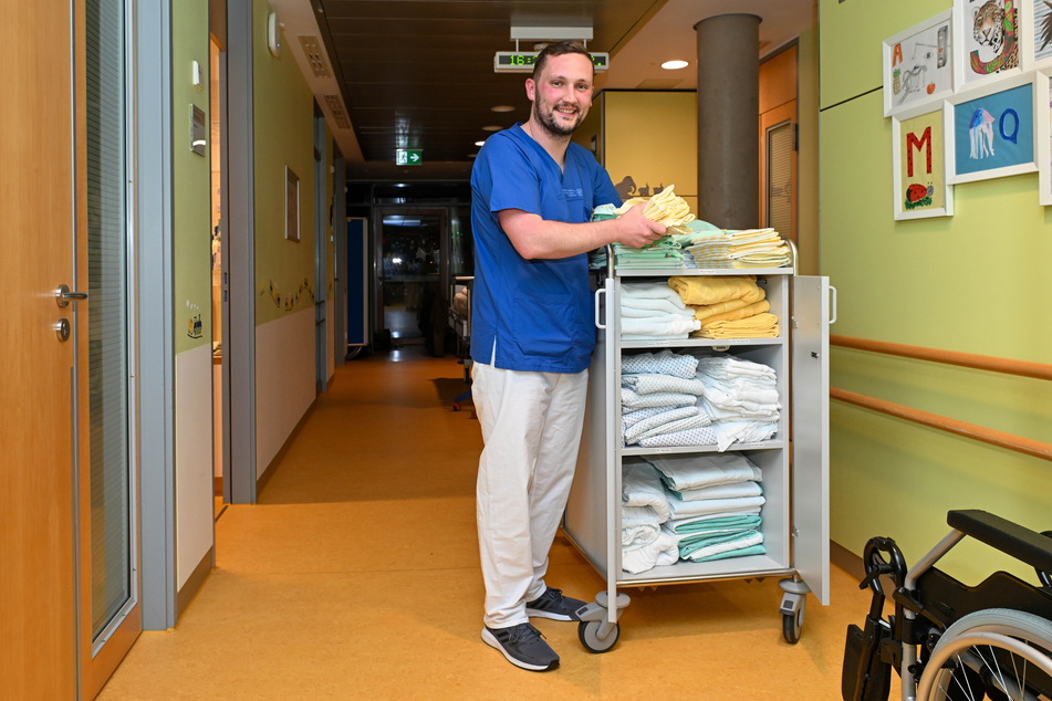 Als Kinderkrankenpfleger ist Sebastian Geisler (33) in blauem Dress und weißer Hose auf der Station unterwegs.