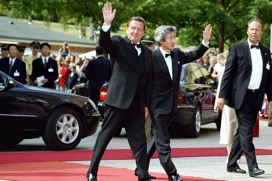 Der damalige Bundeskanzler Gerhard Schröder (SPD) und der damalige japanische Ministerpräsident Junichiro Koizumi winken bei ihrer Ankunft zu den Richard-Wagner-Festspielen im Jahr 2003 in Bayreuth. (Archiv)