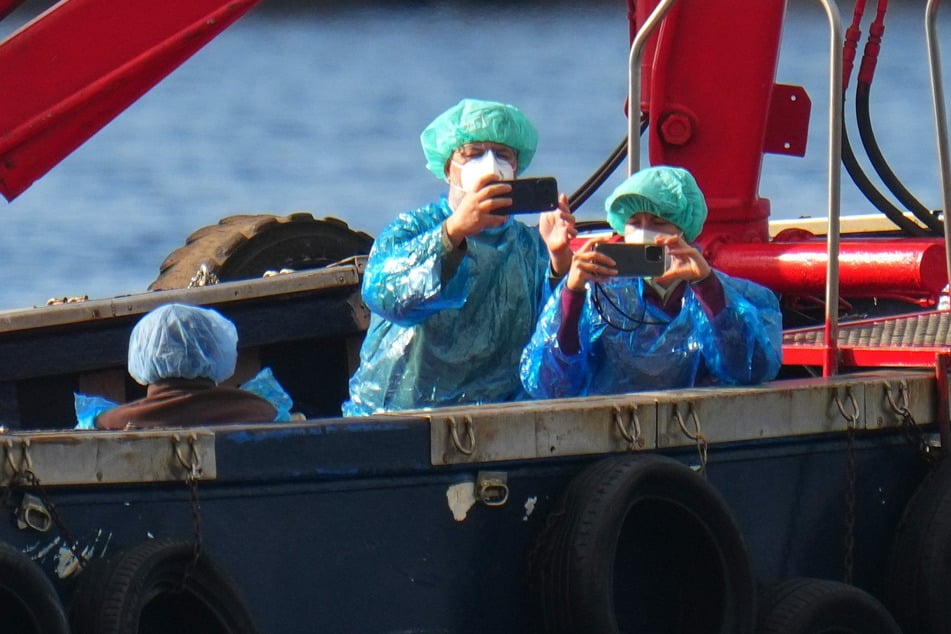 Personen in Schutzbekleidung und mit Masken werden mit einem Boot ausgeschifft.