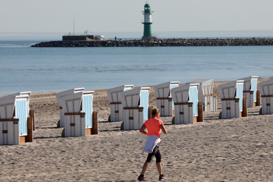 Eine Joggerin sportelt am Strand. Um sie herum stehen Strandkörbe bereit (Symbolbild).