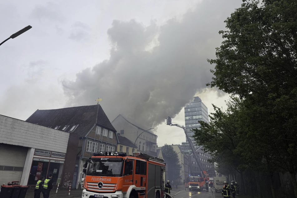 In Hamburg-Harburg steht ein Dachstuhl in Flammen. Über dem Stadtteil steht eine dunkle Rauchwolke.