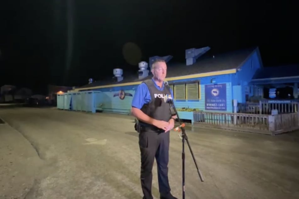 Ein Polizeibeamter hält eine Pressekonferenz in Tatortnähe, vor einem Fischrestaurant.