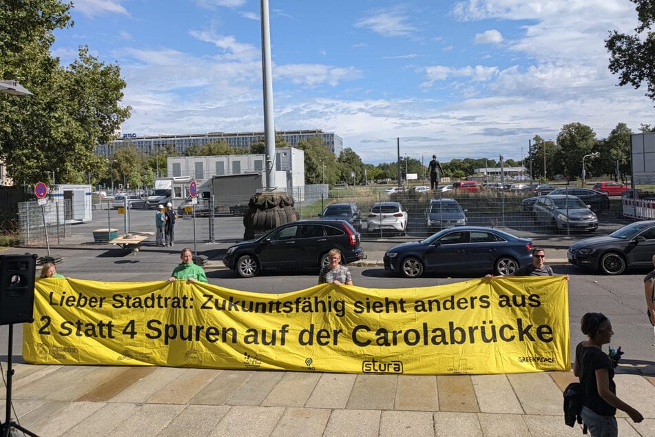 "2 statt 4 Spuren" wird auf einem großen gelben Banner gefordert.