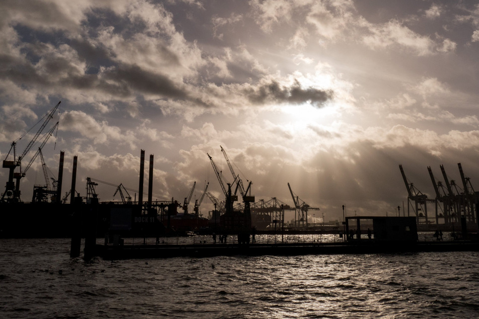 Durch dunkle Regenwolken scheint etwas Sonne über den Hafenanlagen in Hamburg. (Symbolfoto)