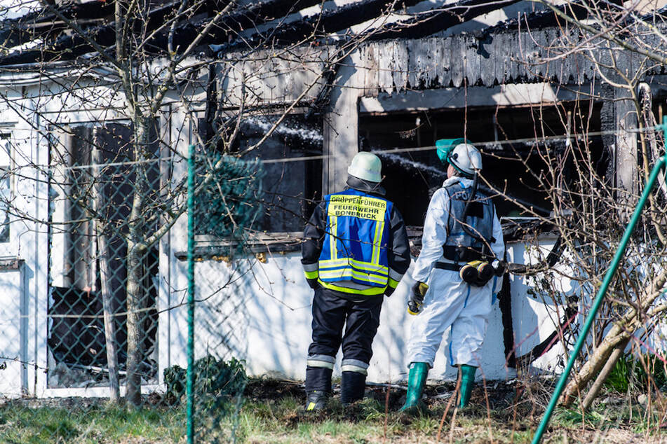 in Polizist (r) und ein Feuerwehrmann stehen vor dem ausgebrannten Einfamilienhaus.