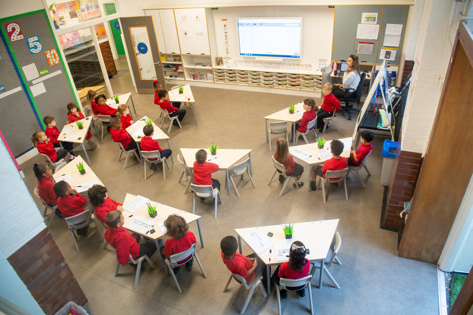 Schülerinnen und Schüler sitzen zusammen mit ihrer Lehrerin in einem Klassenzimmer.