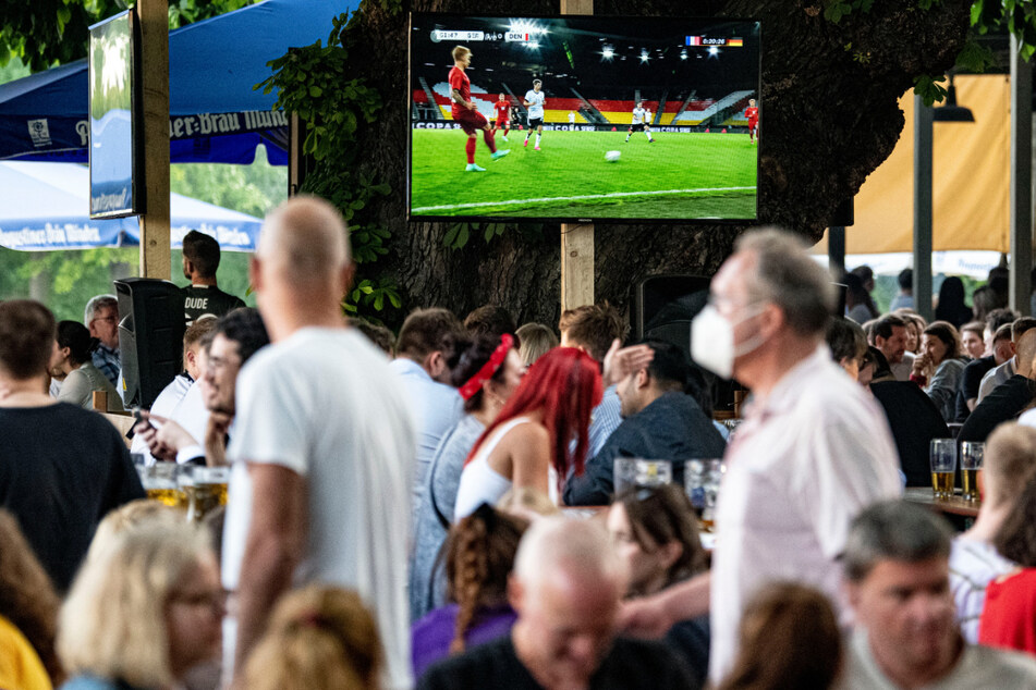 Fans verfolgen bei einem Public Viewing im Zollpackhof die Vorberichterstattung des Spiels auf einem Fernseher.