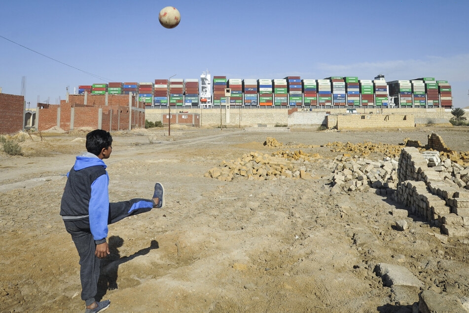 Mit Blick auf das Containerschiff "Ever Given" spielt ein Junge Fußball.