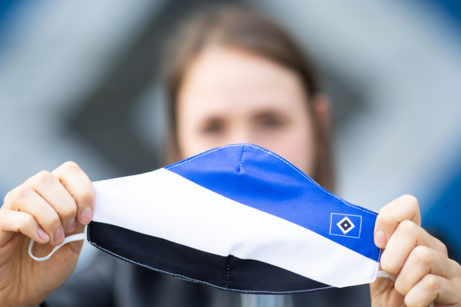 Eine Mitarbeiterin des HSV hält eine Schutzmasken in den Vereinsfarben vor dem Volkspark Stadion.