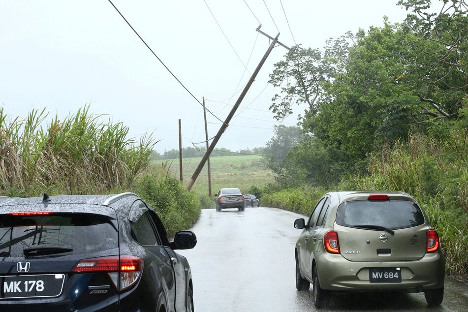 Cars pass a leaning power pole in St. Thomas, Barbados, after Tropical Storm Bret passed north of the island.