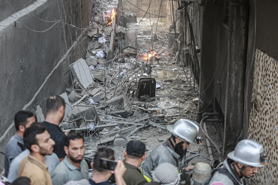 Feuerwehrleute und Anwohner stehen nach einem israelischen Luftangriff vor Trümmern.