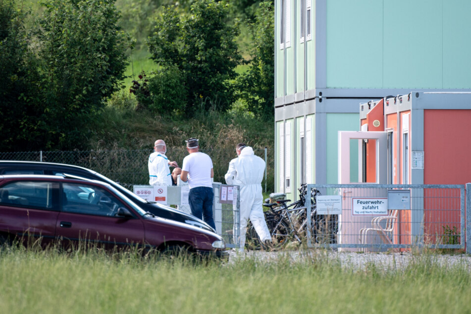 Mitarbeiter vom Landkreis Starnberg stehen in Schutzanzügen am Eingang einer betroffenen Wohncontaineranlage für Flüchtlinge in Pöcking.