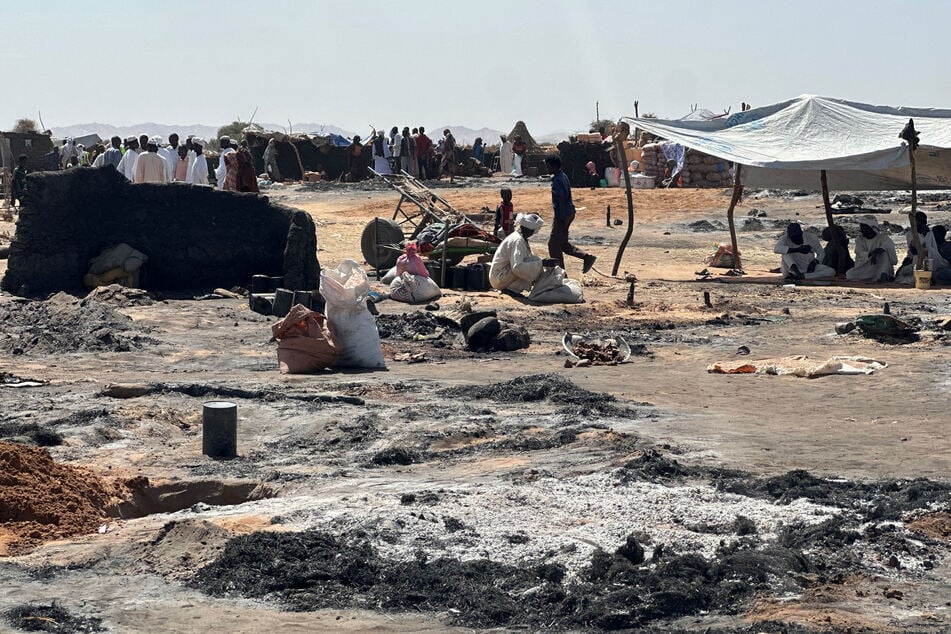 Displaced Sudanese people who left El-Fasher after its fall, sit in the shade in Tawila amid the remains of a fire that broke out in the camp, on February 11, 2026.