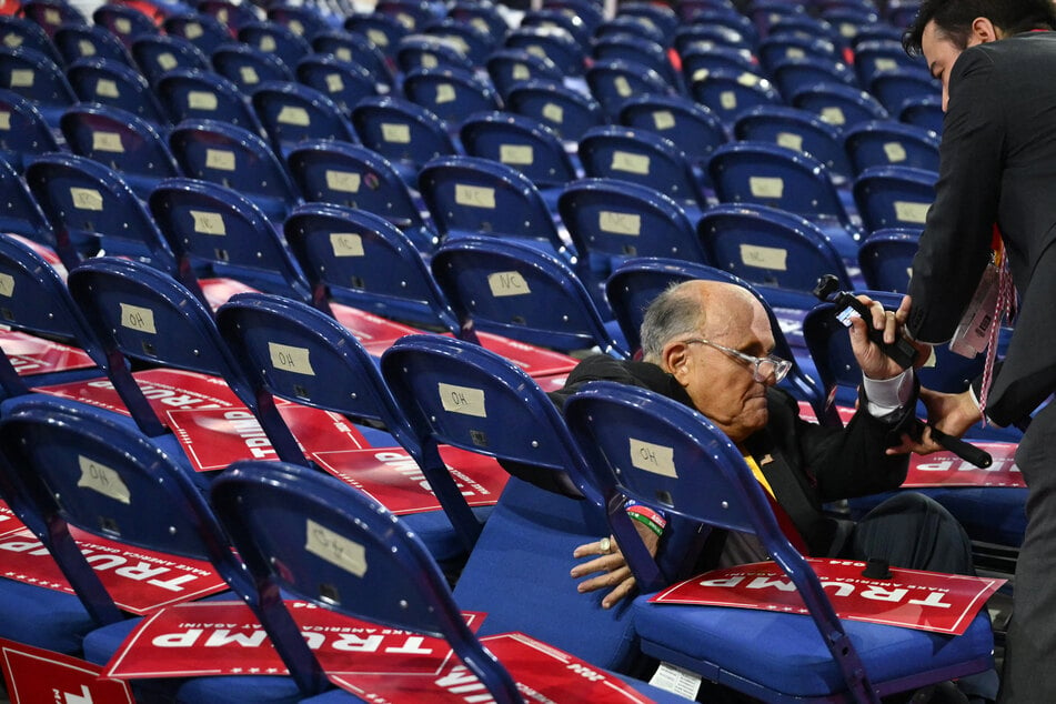 Politician and disbarred lawyer Rudy Giuliani is helped to his feet after falling by walking into a row of chairs on the second day of the 2024 Republican National Convention at the Fiserv Forum in Milwaukee, Wisconsin on Tuesday.