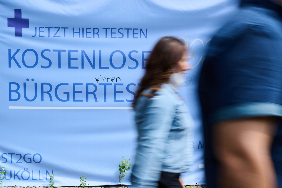"Kostenlose Bürgertests" steht auf einem Plakat während Personen vorüber gehen.