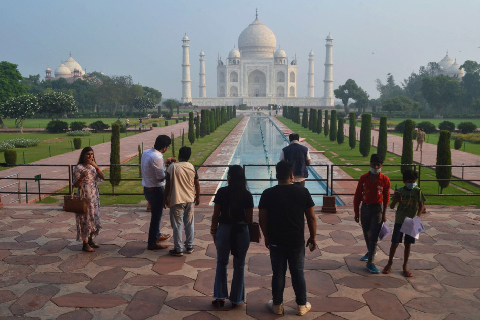 Agra: Touristen stehen am Wasserbecken vor dem Mausoleum Taj Mahal, das im Hintergrund zu erkennen ist.